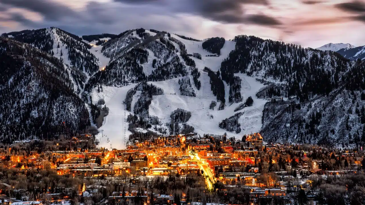 Aspen, Colorado winter landscape with illuminated town, ski slopes, and snow-covered mountains at sunset
