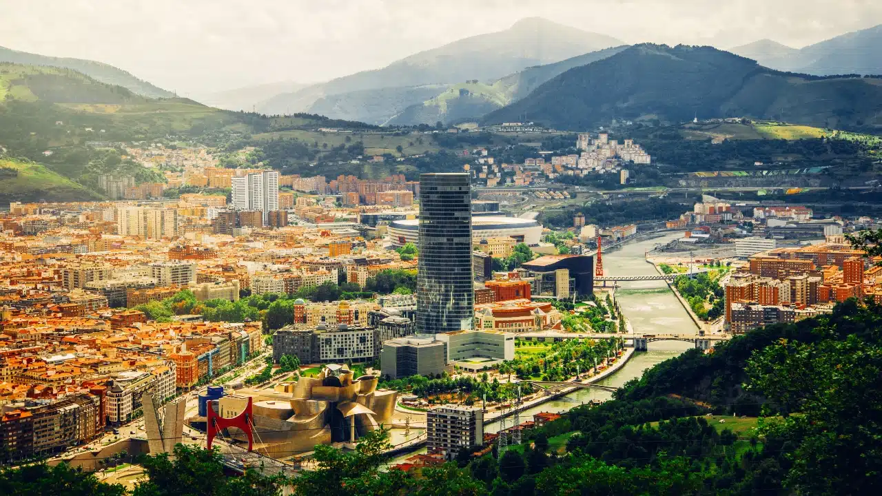 Bilbao cityscape featuring the Guggenheim Museum, Nervión River, modern skyscrapers, and surrounding green mountains in Spain